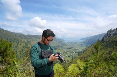 Genç fotoğrafçı kameraya bakıyor. Manzarası çok güzel. Dijital kameralı erkek fotoğrafçı.