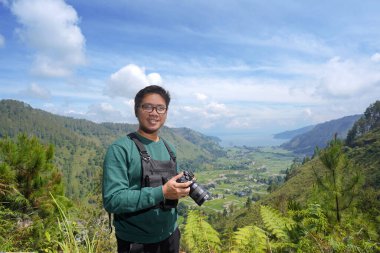 Asyalı fotoğrafçı elinde kamerayla kendine güvenen bir gülümsemeyle
