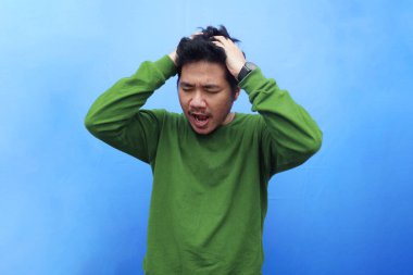 Asyalı genç bir adamın portresi mavi arka planda izole edilmiş çaresiz yüz ifadesi ile hayal kırıklığına uğramış hissediyor.