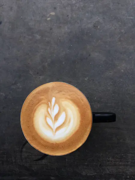 stock image Close-up photo of a cappuccino with latte art in a ceramic cup on a concrete table. The latte art design resembles a rosetta.