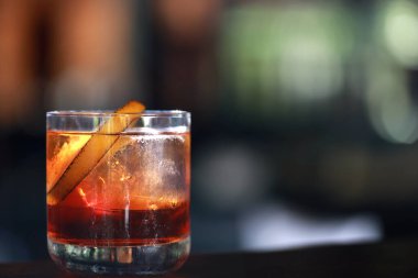 Klasik bir kokteylin yakın plan çekimi, muhtemelen bir Negroni ya da benzer bir içki, düşük bardakta. İçkinin kehribar kırmızısı renkli ve portakal kabuğuyla süslenmiş..