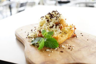 Patlamış muz tatlısının olduğu bir tabağın yakın plan fotoğrafı. Altın-kahverengi muz boydan boya dilimlenir ve üzerine zengin bir çikolata sosu ve rendelenmiş peynir serpiştirilir..