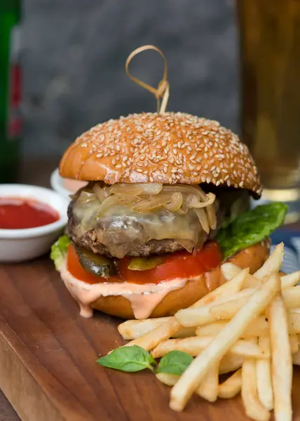 stock image A close-up image of a gourmet cheeseburger served on a wooden board. The burger features a sesame seed bun, melted cheese, caramelized onions, tomato, lettuce, and pickles. 