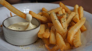 Görüntü, ağız sulandıran bir tabak patates kızartması gösteriyor. Altın sarısı ve çıtır çıtır, patatesler bol bol bitki ya da peynir serpiştiriliyor..