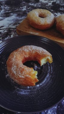 Görüntü, unla kaplı koyu bir yüzey ve birkaç pişmemiş çöreğin üst üste dizilmiş halini gösteriyor. Çörekler soluk sarı ve ortada belirgin bir delik var..