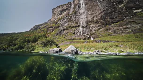 フィヨルドのオーバーアンダーシュート 太陽のフレアは雑草で覆われた底で踊る 岩の多い崖から滝がカスケード 高品質4K映像 — ストック動画