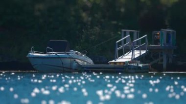 A motorboat moored in the small dock. Sun shimmers on the water creating bright flares. Slow-motion,pan left. High quality 4k footage