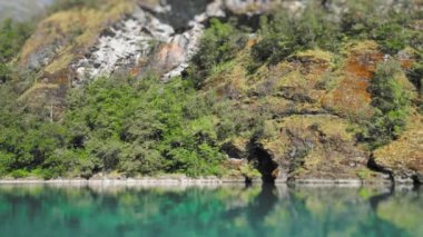 Forest-covered rocky cliffs above the Loenvatnet lake reflected in the still water. Slow-motion, view from the water. High-quality 4k footage