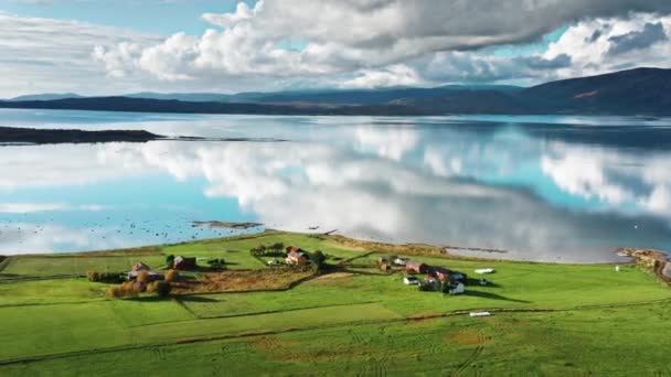 穏やかな鏡のようなフィヨルドの緑の海岸にある小さな村や農場 穏やかな海に白い雲が反映されます 空中からの眺め パン左 高品質4K映像 — ストック動画