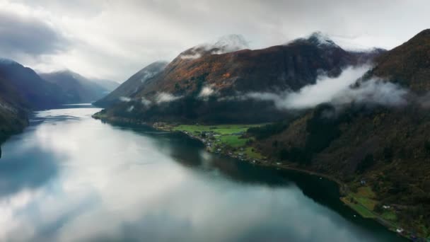 从空中俯瞰峡湾绿色海岸上的小村子 背景中的低云和高山 空中风景 高质量的4K镜头 免版税图库视频
