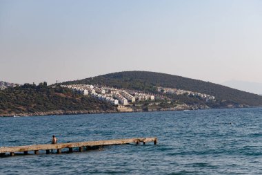 Denizden Kusadasi 'ye yerleşim yeri manzarası, Türkiye' de denize bakan bir çocukla birlikte bir iskeleye sahip..