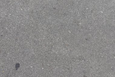 Küçük kayalar ve dokularla gri beton bir yüzeye yakın çekim. Bir karanlık nokta görünüyor..