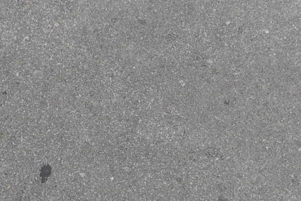 Küçük kayalar ve dokularla gri beton bir yüzeye yakın çekim. Bir karanlık nokta görünüyor..