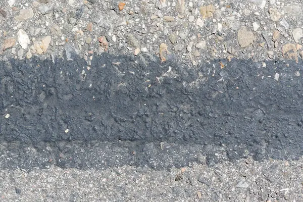 Açık dokulu çakıllara karşı yatay koyu bir çizgi içeren asfalt yüzeyinin yakın çekimi.