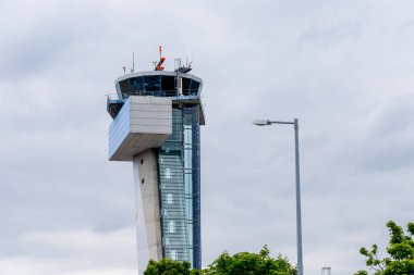 Nuremberg, Almanya - 25 Mayıs 2025: Görüntü, bulutlu bir gökyüzüne karşı bir havaalanı kontrol kulesine sahip, alt tarafında sokak lambası ve yeşil yeşillikler bulunuyor.