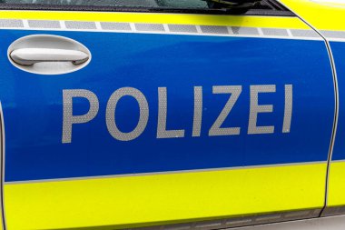 Nuremberg, Almanya - 25 Mayıs 2025: Yansıtıcı harfler, mavi arkaplan ve sarı çizgili bir polis aracının yan görüntüsü. Su damlacıkları görünür..