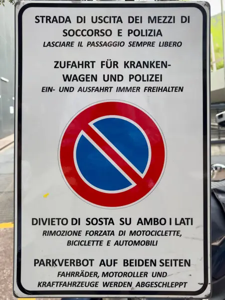 İtalya, 23 Nisan: Acil durum araçları için park yasağı olduğunu belirten İtalyanca ve Almanca bir metinle imzalayın. Kırmızı ve mavi bir park sembolü içermiyor..