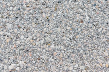 Tam kare yakın plan, çeşitli renk ve şekillerde küçük kayalar ile gömülü açık gri beton bir yüzey gösteriyor..