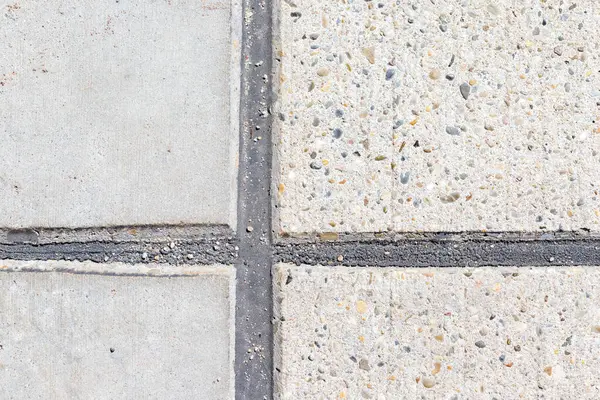 Koyu gri dolgu maddesiyle ayrılmış dört beton kaldırım karesinin yukarıdan çekimi. İki kare pürüzsüz, ikisi çakıl desenli..
