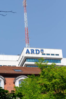 Münih, Almanya - 14 Haziran 2025: Almanya 'daki ARD binasının alçak açılı görüntüsü kırmızı ve beyaz bir anten kulesiyle açık mavi gökyüzüne karşı, kısmen ağaçlarla gizlenmiş.