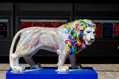 Münih, Almanya - 14 Haziran 2025: Resmi bir aslan heykeli mavi bir platformun üzerinde duruyor, kelimeler ve renkli işaretlerle süslenmiş, poster sergilenen bir binaya karşı..