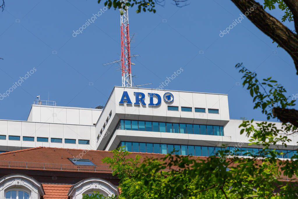 Munich, Germany - June 14 2025: The image shows the ARD building under a blue sky, framed by tree branches. The building has a red and white communications tower.