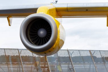 Nuremberg, Almanya - 25 Mayıs 2025: Bir kanada bağlı sarı ve gri bir uçak motorunun yakın çekimi. Motor, bulutlu bir gökyüzüne ve havaalanı çitlerine karşı çerçeveye hükmediyor.