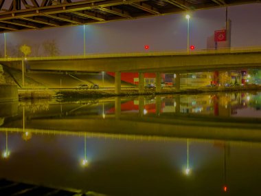 Nuremberg, Almanya, 2025 Şubat 20: Liman: Su üzerindeki beton köprülerin gece görüşü, görülebilir yansımaları. Binalar ve sokak lambaları kıyı boyunca uzanır. Çelik köprü yapısı.