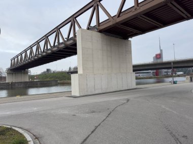 Nuremberg, Almanya 2024 Novenber 14: Harbour: Görüntü nehir üzerindeki beton iskelelerin üzerinde çelik bir kiriş köprüsü gösteriyor. Önde bir yol var. Arka planda bulutlu gökyüzü ve sanayi binaları görülüyor.