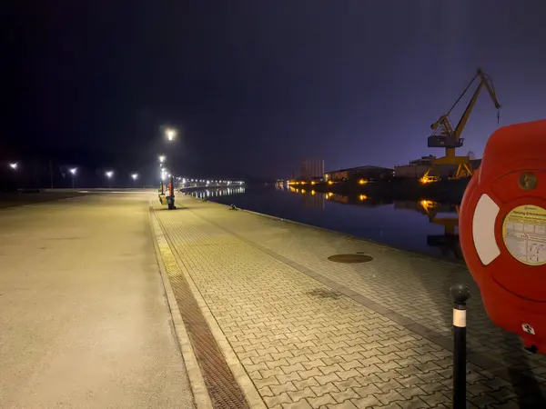 Nuremberg, Almanya 2025 Şubat: Limanın 20 Şubat: Gece sahnesinde deniz kenarında sokak lambaları, vinç ve liman binaları suya yansıyor. Kırmızı güvenlik ekipmanları ön planda.