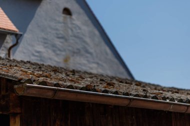 Eski, yosunlu, hendeği olan bir çatı, açık mavi bir gökyüzünün arka planına ve bulanık bir bina cephesine karşı kurulmuş..