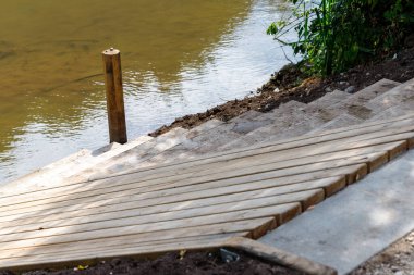 Tahta basamaklar bir su kütlesinden çimenli bir bankaya götürür. Tek bir tahta direk suyun kenarında duruyor..