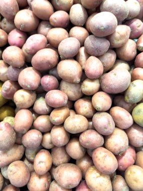 Yakın plan çekimde yoğun bir şekilde paketlenmiş ve çerçeveyi dolduran büyük bir kırmızı patates yığını görülüyor. Pembe, kırmızı ve bronzlaşmış renkler görülebilir..