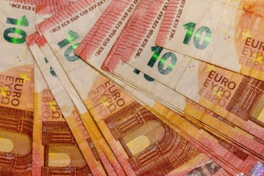 Yakın plan, birkaç üst üste on Euro 'luk banknotun hafif açılı çekimi. Baskın renkler sarı, turuncu ve kırmızıdır.
