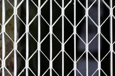 Beyaz metal bir kapıya yakın çekim veya elmas şekilli delikleri olan ızgara, karanlık, odak dışı bir arka plan üzerine kuruludur..