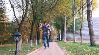 Baba, oğlunu yol boyunca parkta taşıyor. Yakın çekim yüksek kalite 4K görüntü