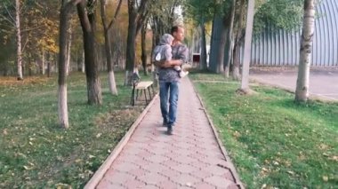 Baba, oğlunu yol boyunca parkta taşıyor. Yakın çekim yüksek kalite 4K görüntü