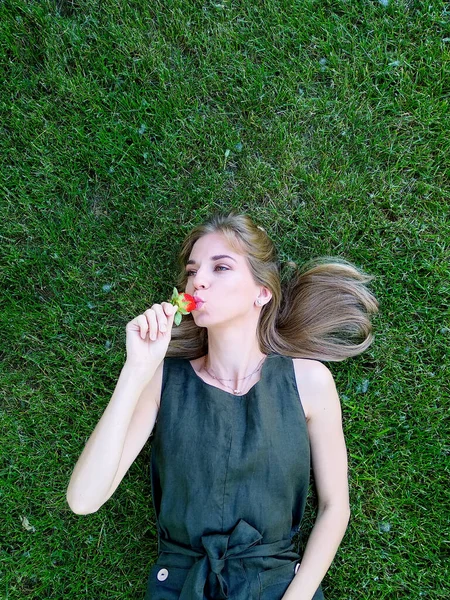 Güzel bir kadın çimlere uzanıyor ve çilek tadı alıyor. Yüksek kalite fotoğraf