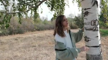 Genç ve güzel bir kadın huş ağacına sarılıyor. Yüksek kalite 4k görüntü