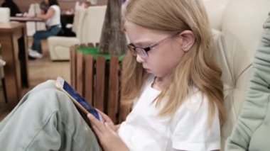 Gözlüklü bir kız bir kafedeki kanepede oturur ve akıllı telefona bakar. Yüksek kalite 4k görüntü