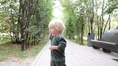 Şirin küçük çocuk parkta yolda duruyor ve gülümsüyor. Yüksek kalite 4k görüntü