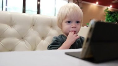 Küçük şirin çocuk bir kafede oturur ve akıllı telefon ekranına bakar. Yüksek kalite 4k görüntü