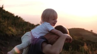Father sits his son on his shoulders at sunset in the mountains. High quality 4k footage