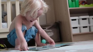 Sevimli küçük tüylü çocuk beşiğin yanında yerde oturuyor ve kitap okuyor. Yüksek kalite 4k görüntü