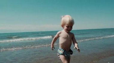 Little cute boy playing along the shore with waves. High quality 4k footage