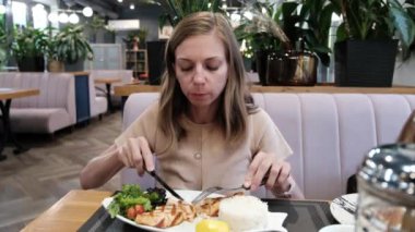 A young woman sits in a restaurant and eats a dish of salmon. High quality 4k footage