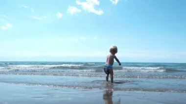 Little cute boy playing along the shore with waves. High quality 4k footage