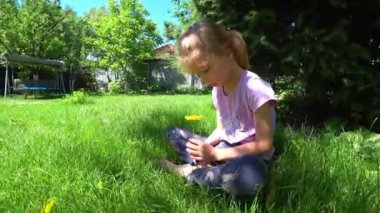 Portrait of a little sad girl sits on the lawn under the spruce. High quality 4k footage