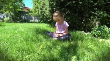 Portrait of a little sad girl sits on the lawn under the spruce. High quality 4k footage