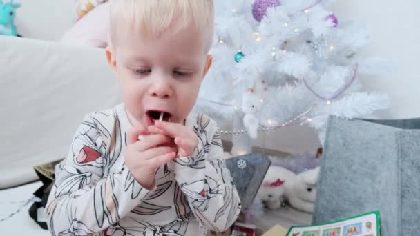 Malý Roztomilý Chlapec Kouše Lízátko Pozadí Bílého Vánočního Stromečku Vysoce — Stock video